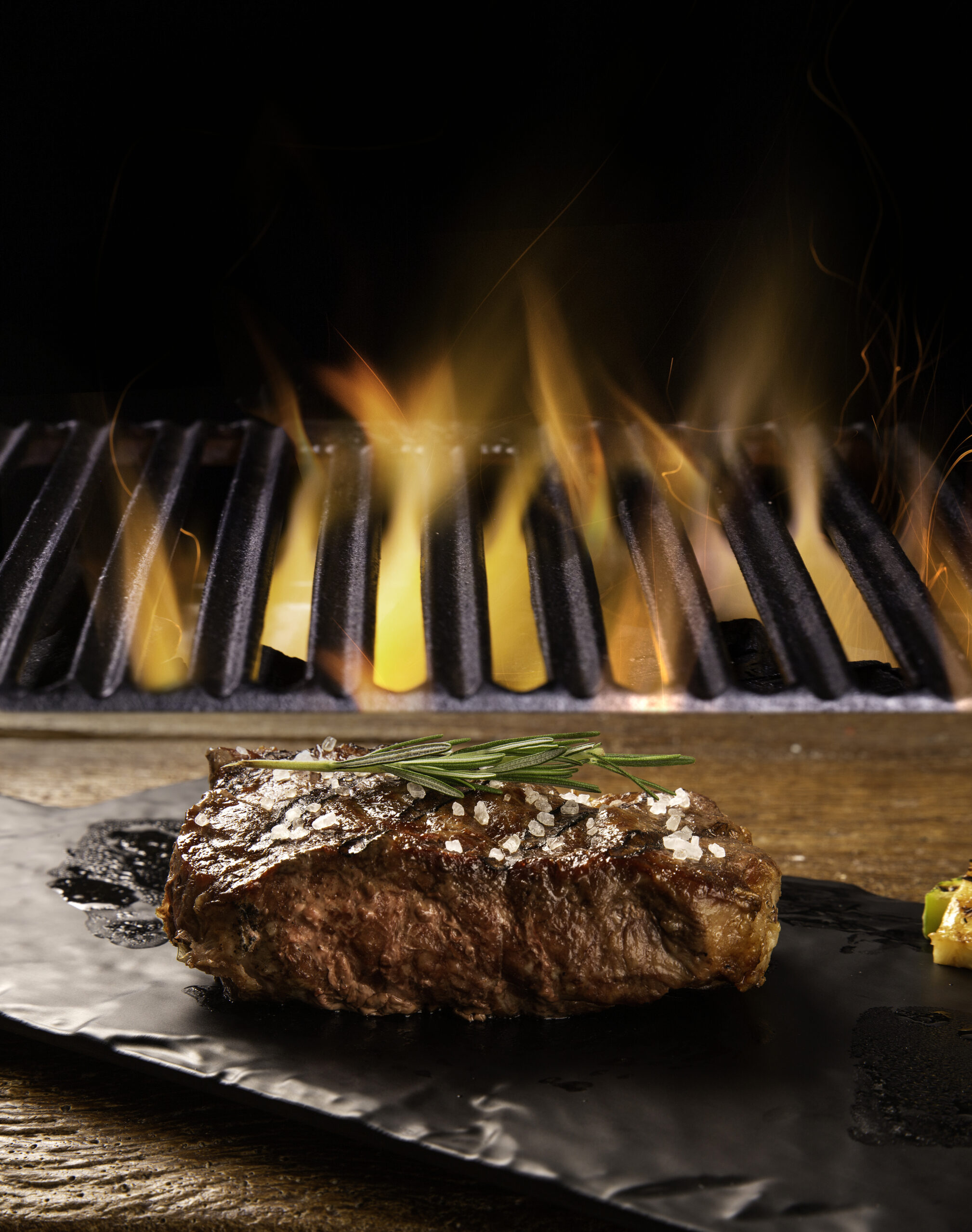 Beef Steak On The Cutting Board With Grill With Fire Background.